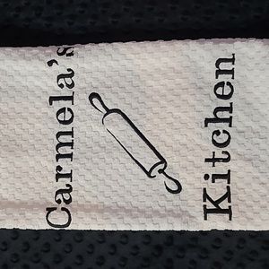 Embroidered dish towel with the name Carmela's on it.